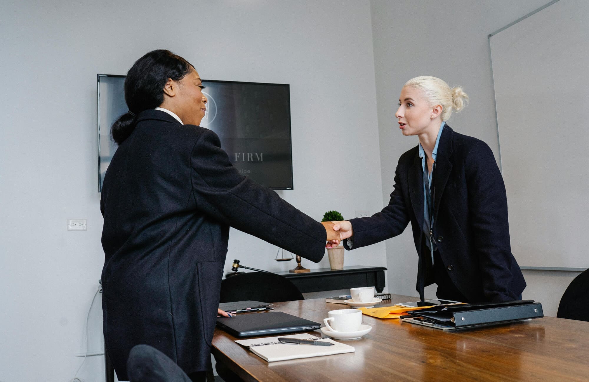 Two office workers shaking hands over a wooden desk.