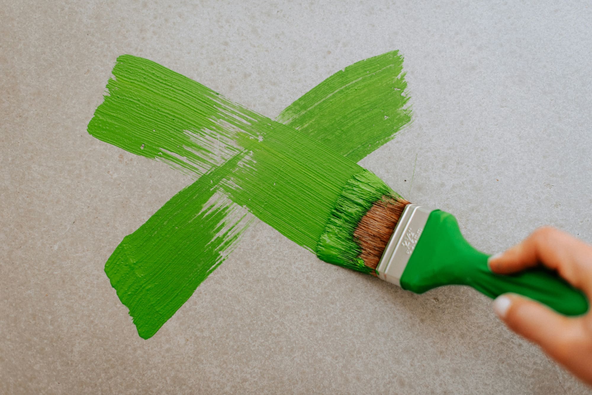 Paintbrush painting a green 'X' in to a grey wall.