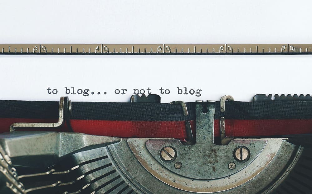 A typewriter typing the words 'to blog... or not to blog' on piece of paper.