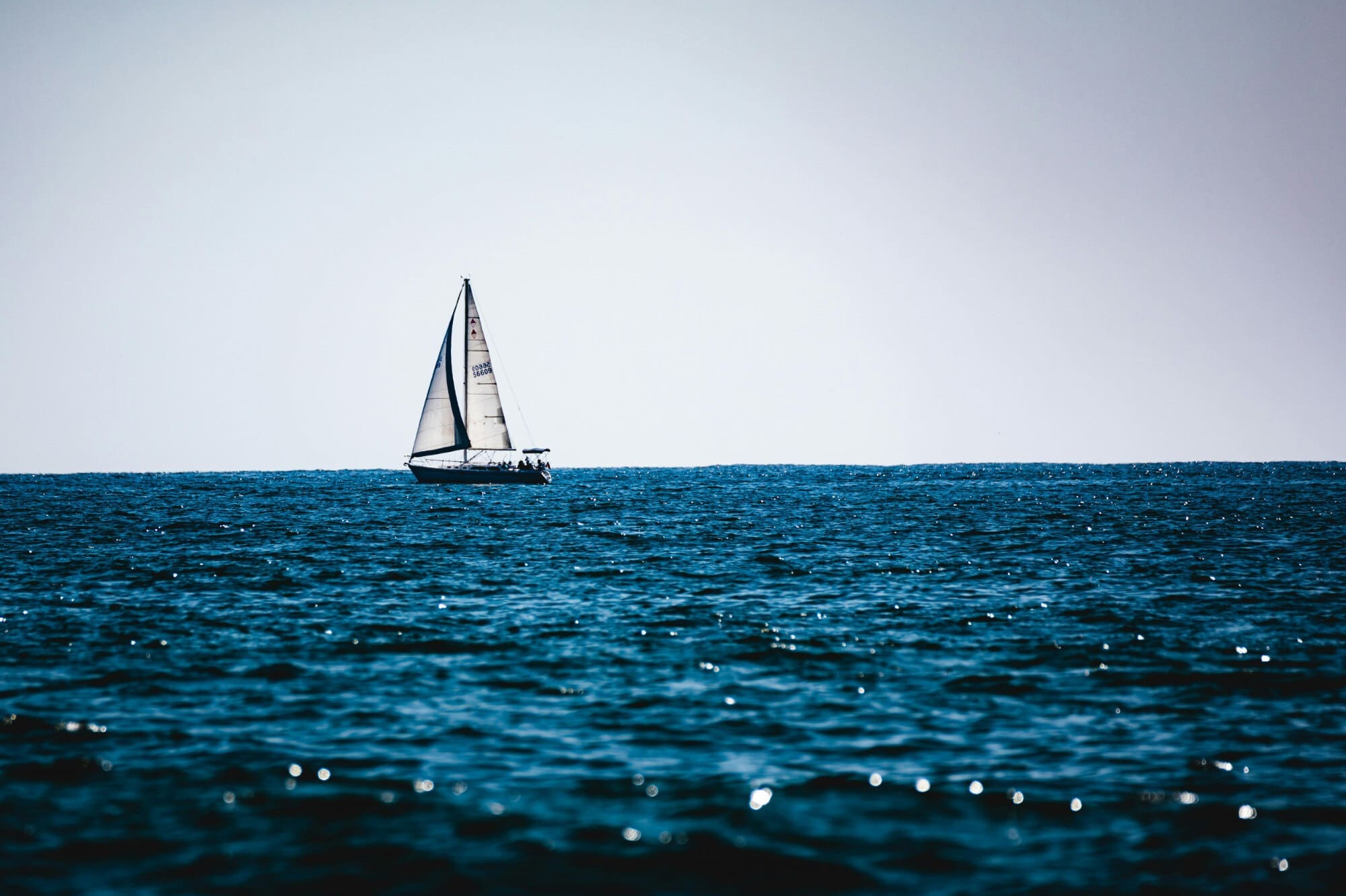 A small sail boat near the horizon in front of a body of water.