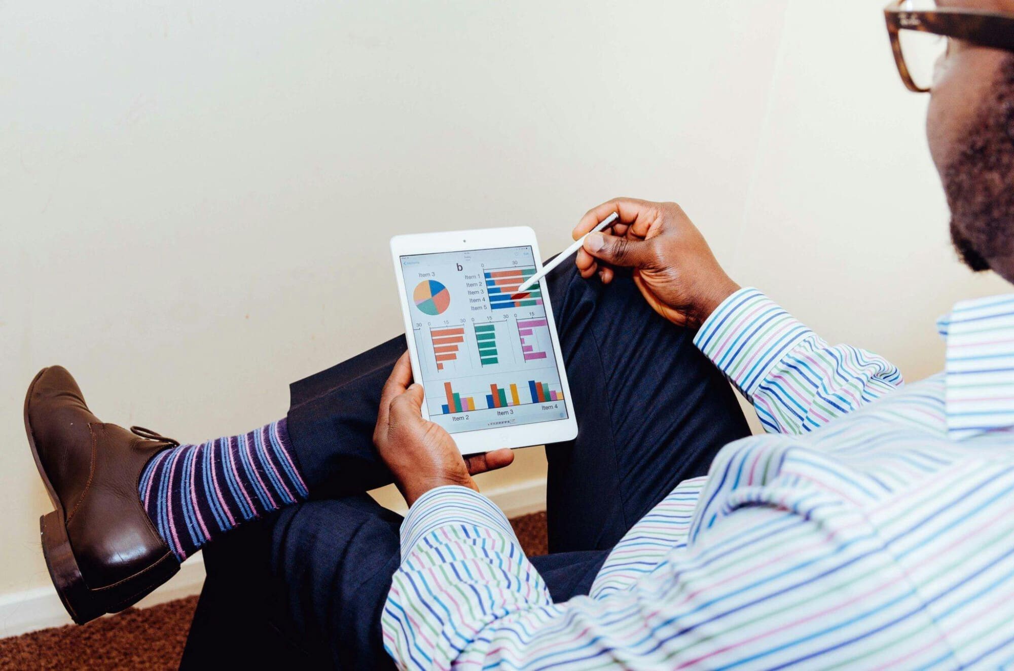 Man in business attire sitting down, pointing a pen towards business graphs on a tablet.