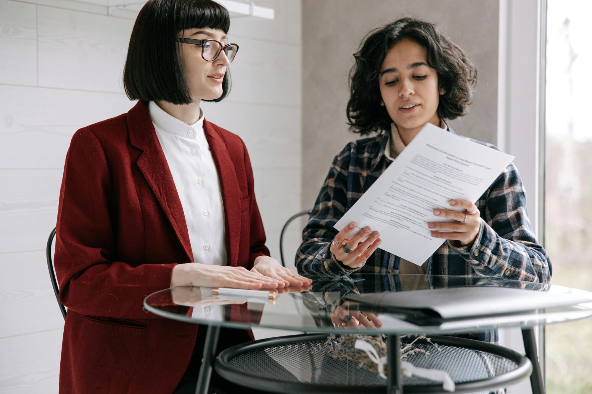 Two people behind round glass table looking at a paper document.