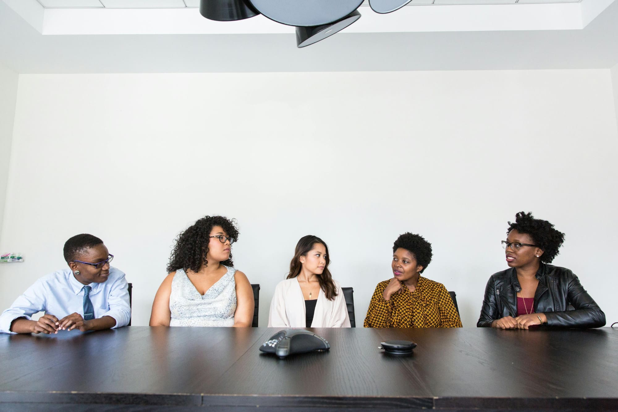 Five people sat side by side at dark wooden desk in office.