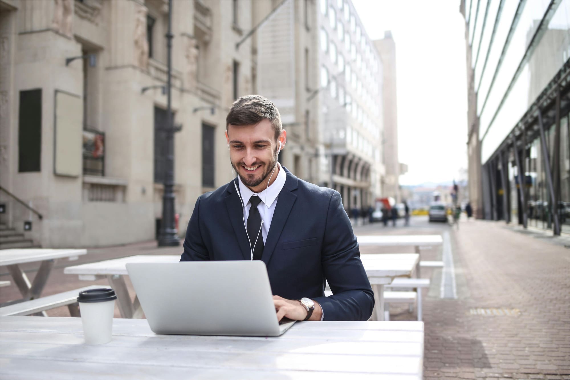 Freelancer working on laptop at outdoor bench with street in the background.