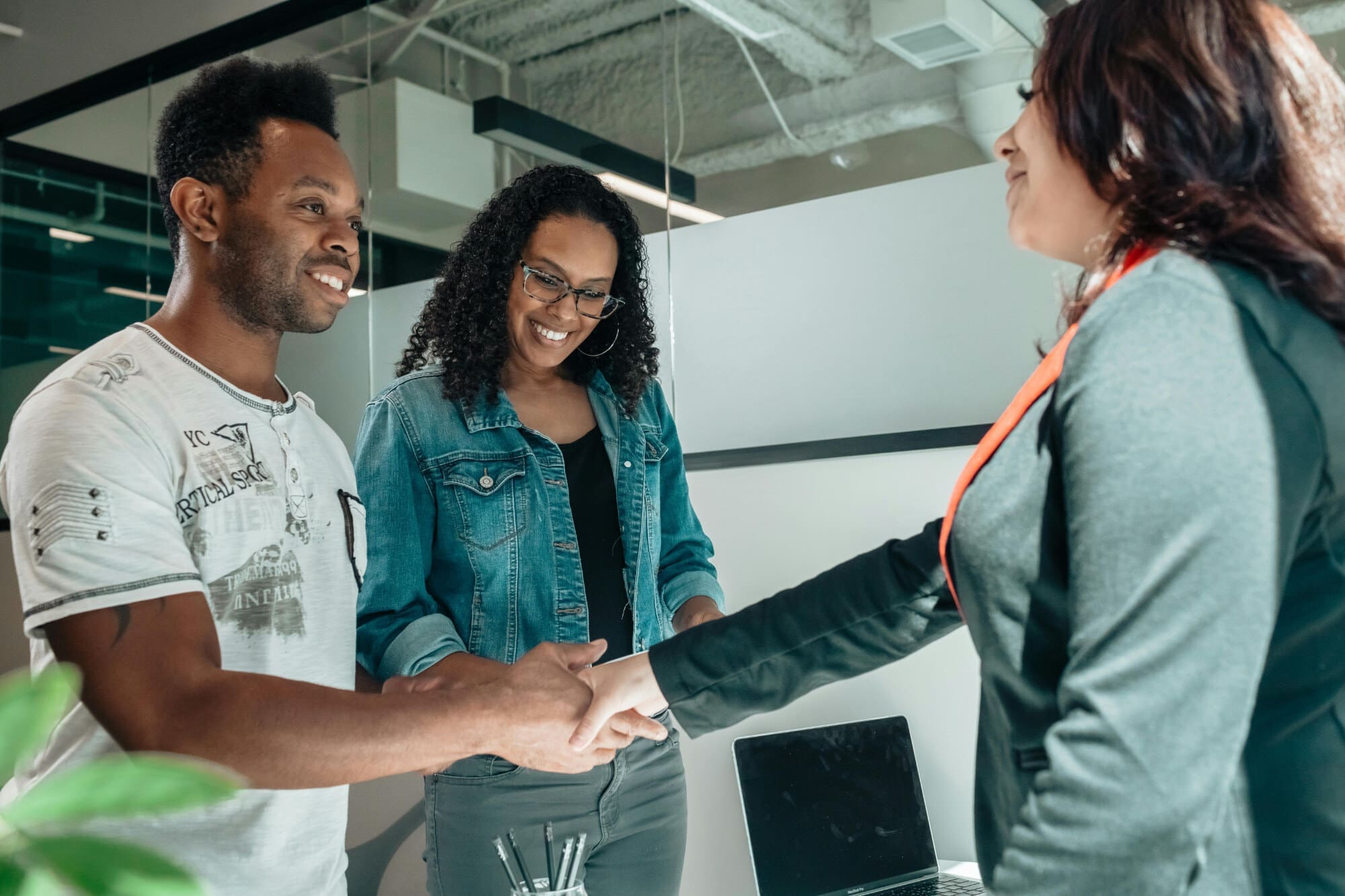 Two people shaking hands in an office with one person looking on.