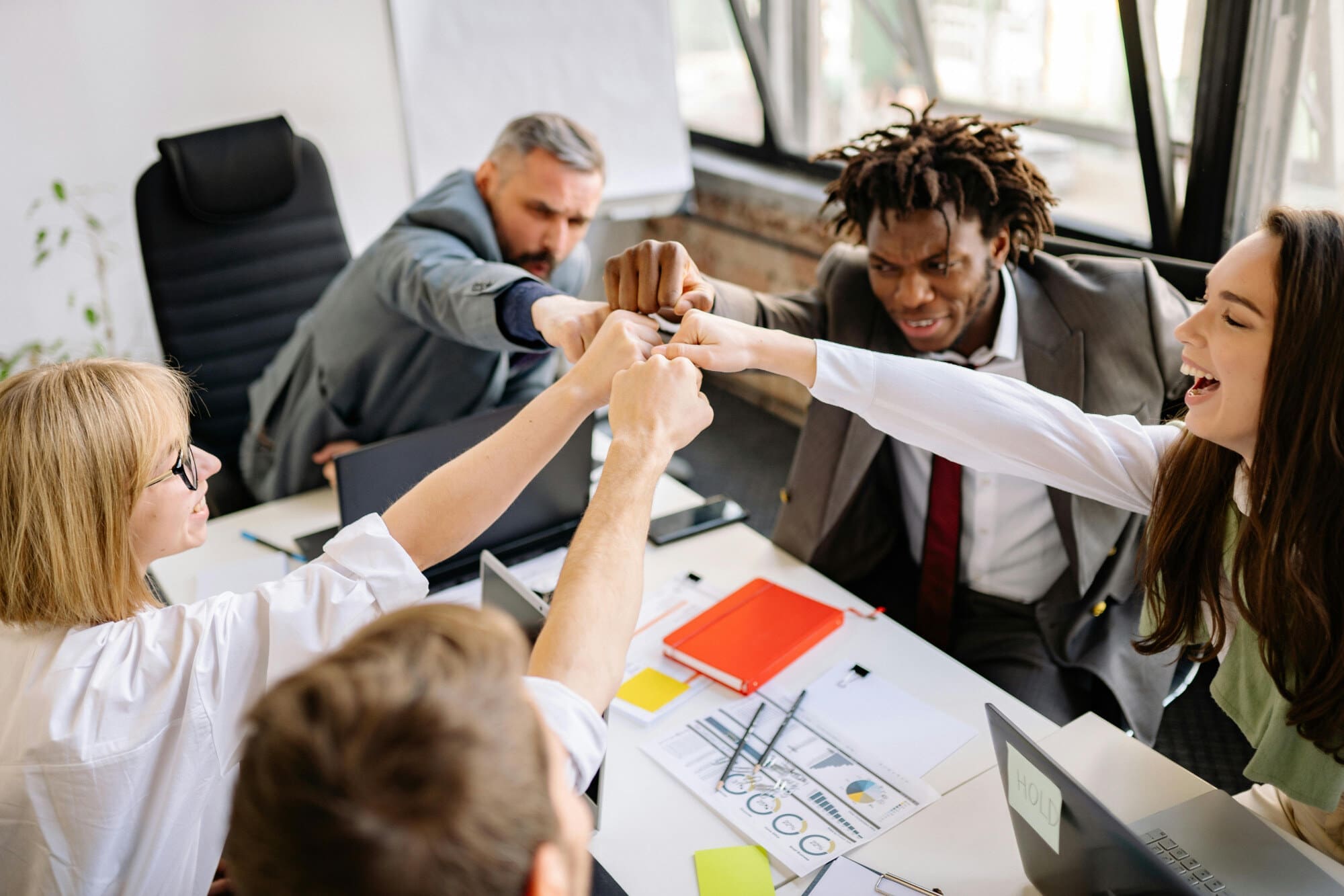 Office workers sitting around table and celebrating by fist bumping each other.