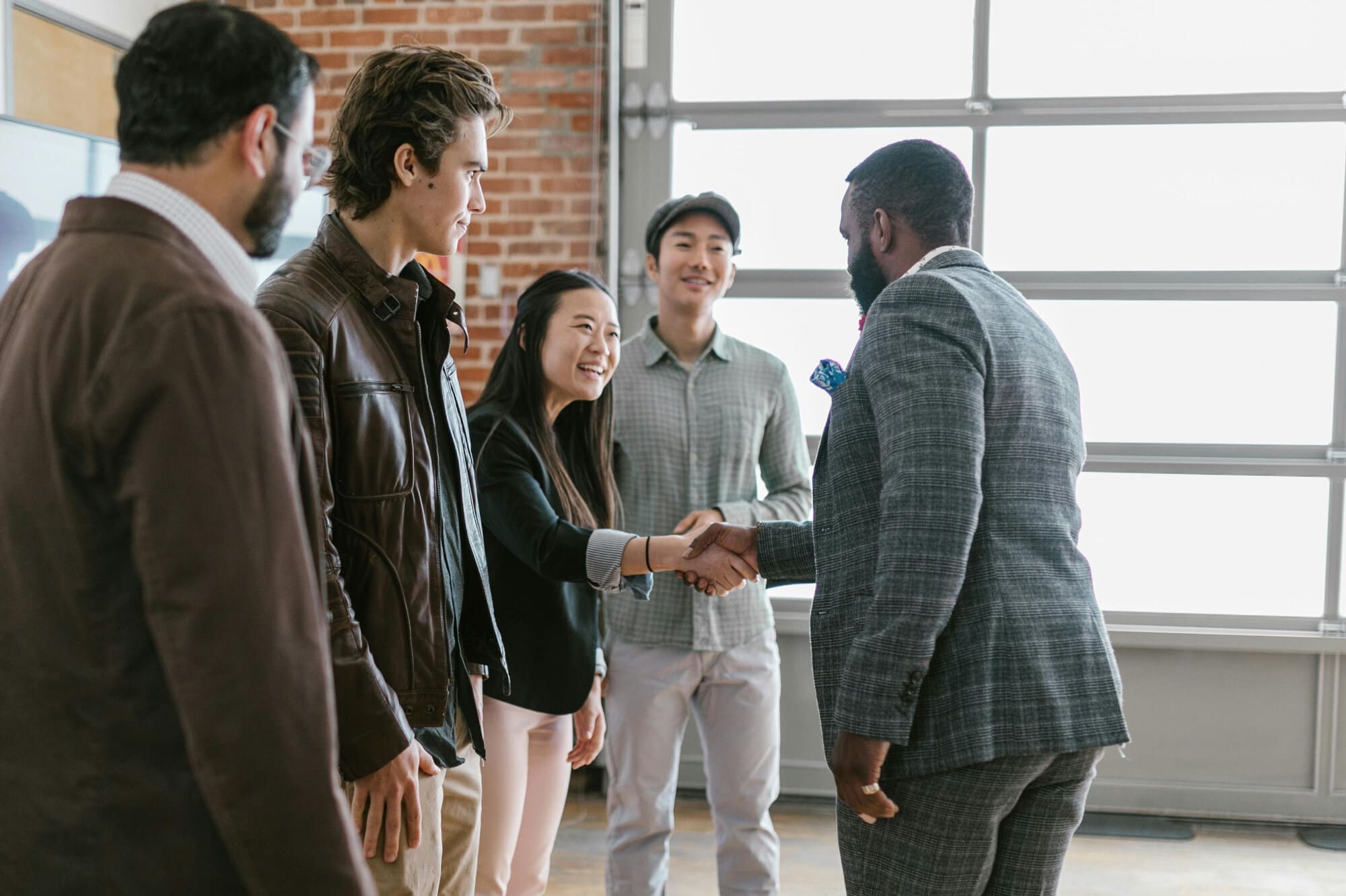 Group of office workers standing around two people shaking hands.