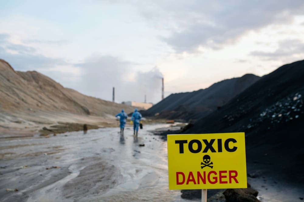 Sign saying 'Toxic/Danger' in front of barren landscape and factory.