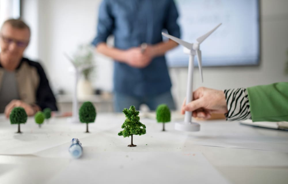 A table in an office with various sustainability-related model items on it including trees and a wind turbine.