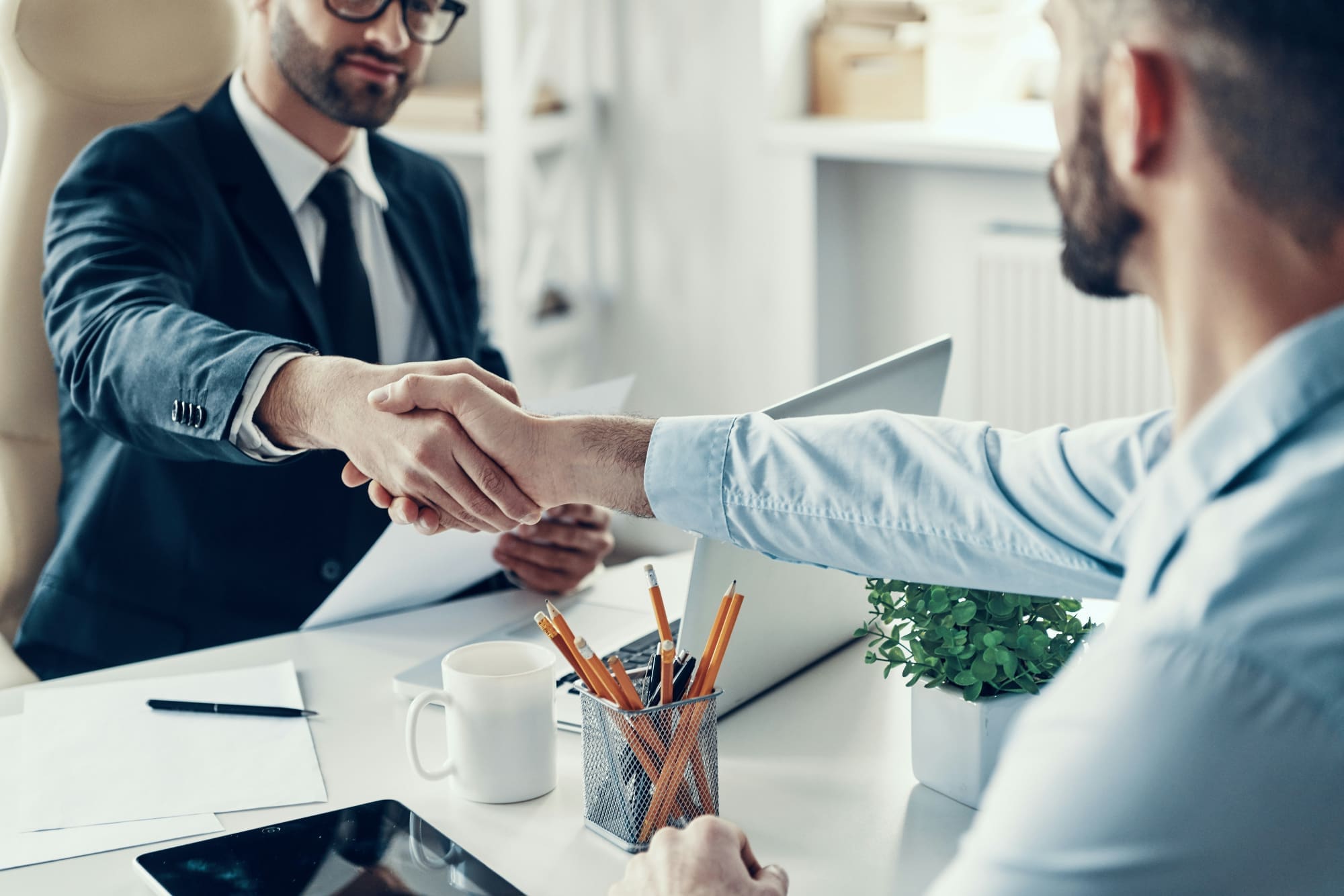 Dazzle can help with ESG recruitment Two office workers shaking hands over a white desk