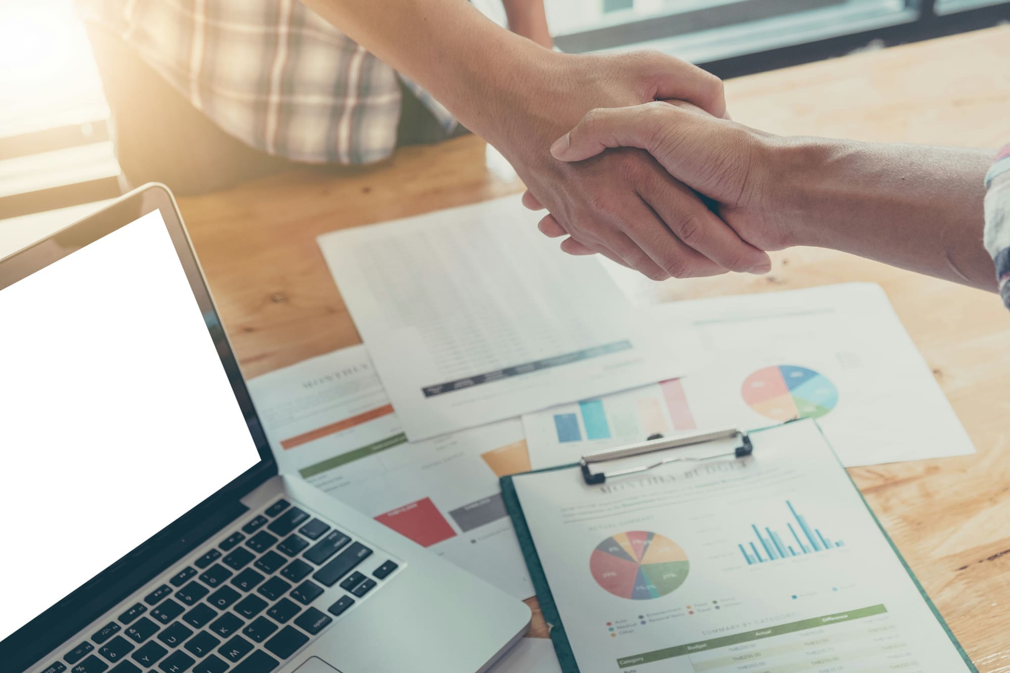 Dazzle's customizable sustainability services Two business people shaking hands over business charts sitting on desk.