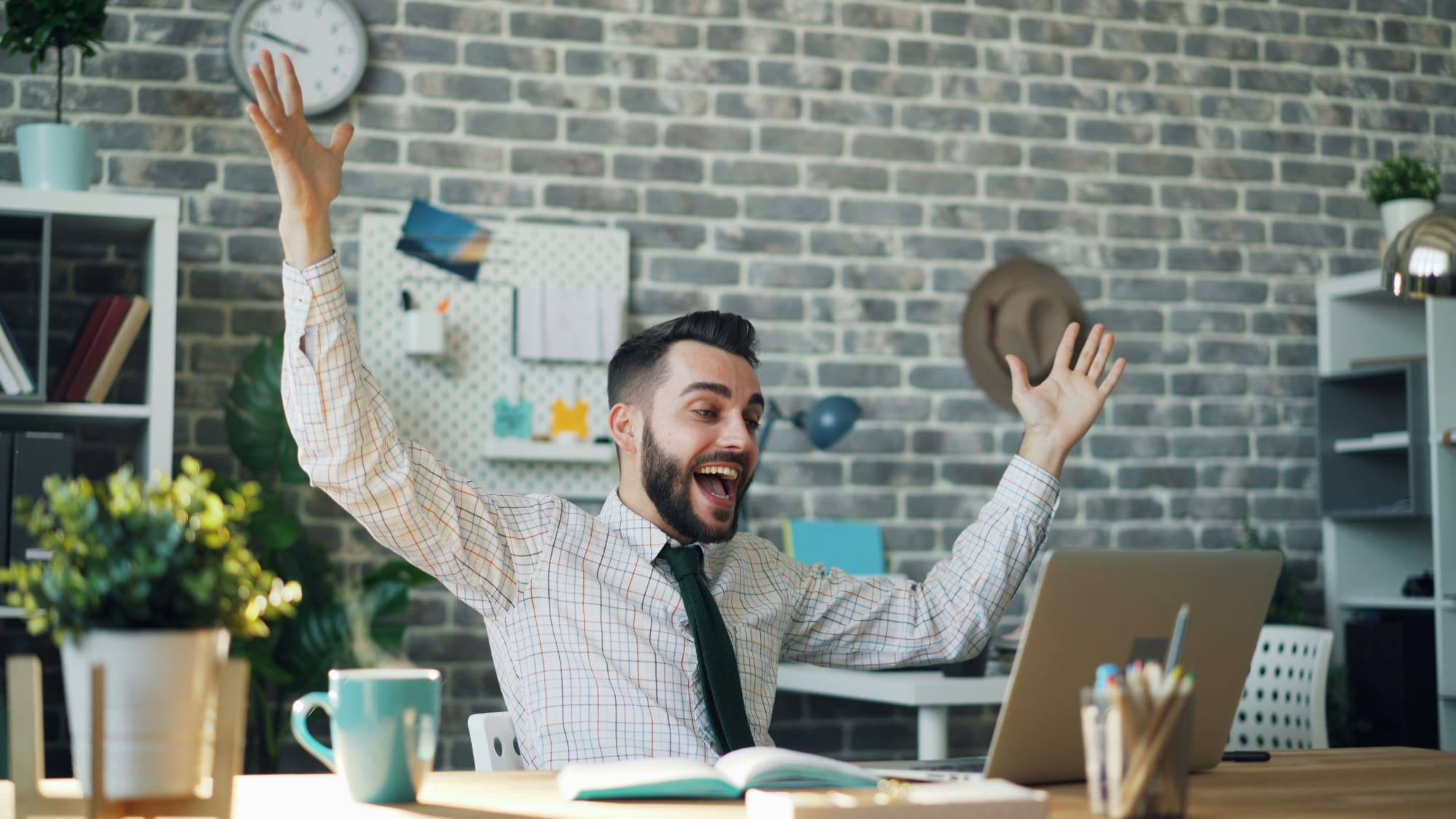 Delighted! Office worker celebrating at desk with hands in the air.