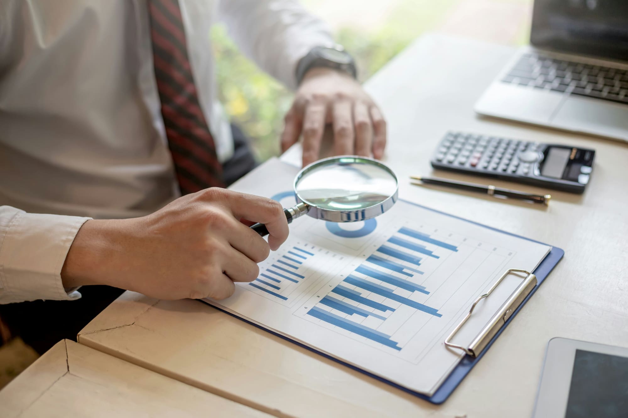 Find sustainability services A business person sitting at desk using magnifying glass to look at business charts.