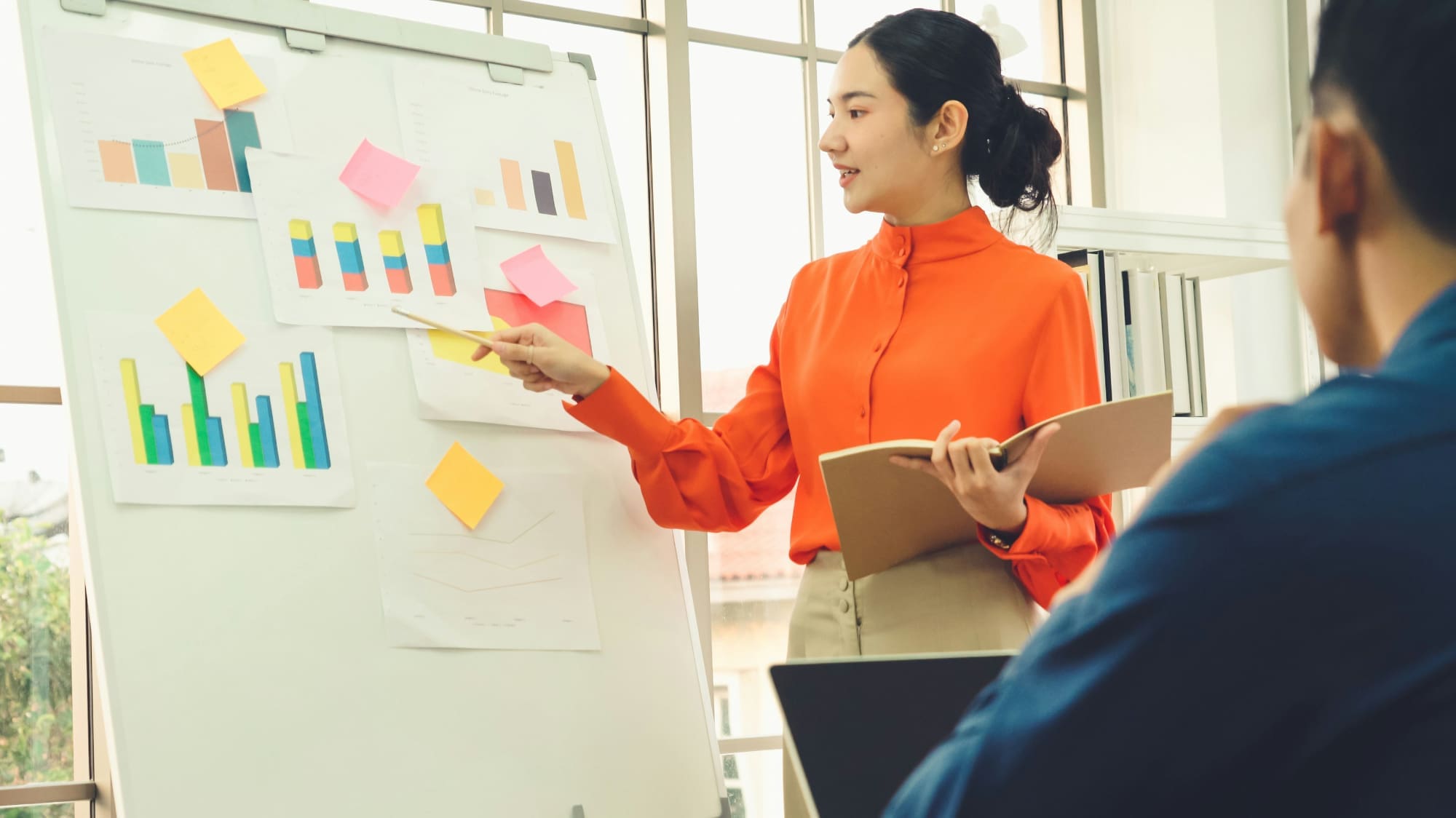 Sustainability Goals Progress Woman pointing to whiteboard covered in business charts with man looking on.