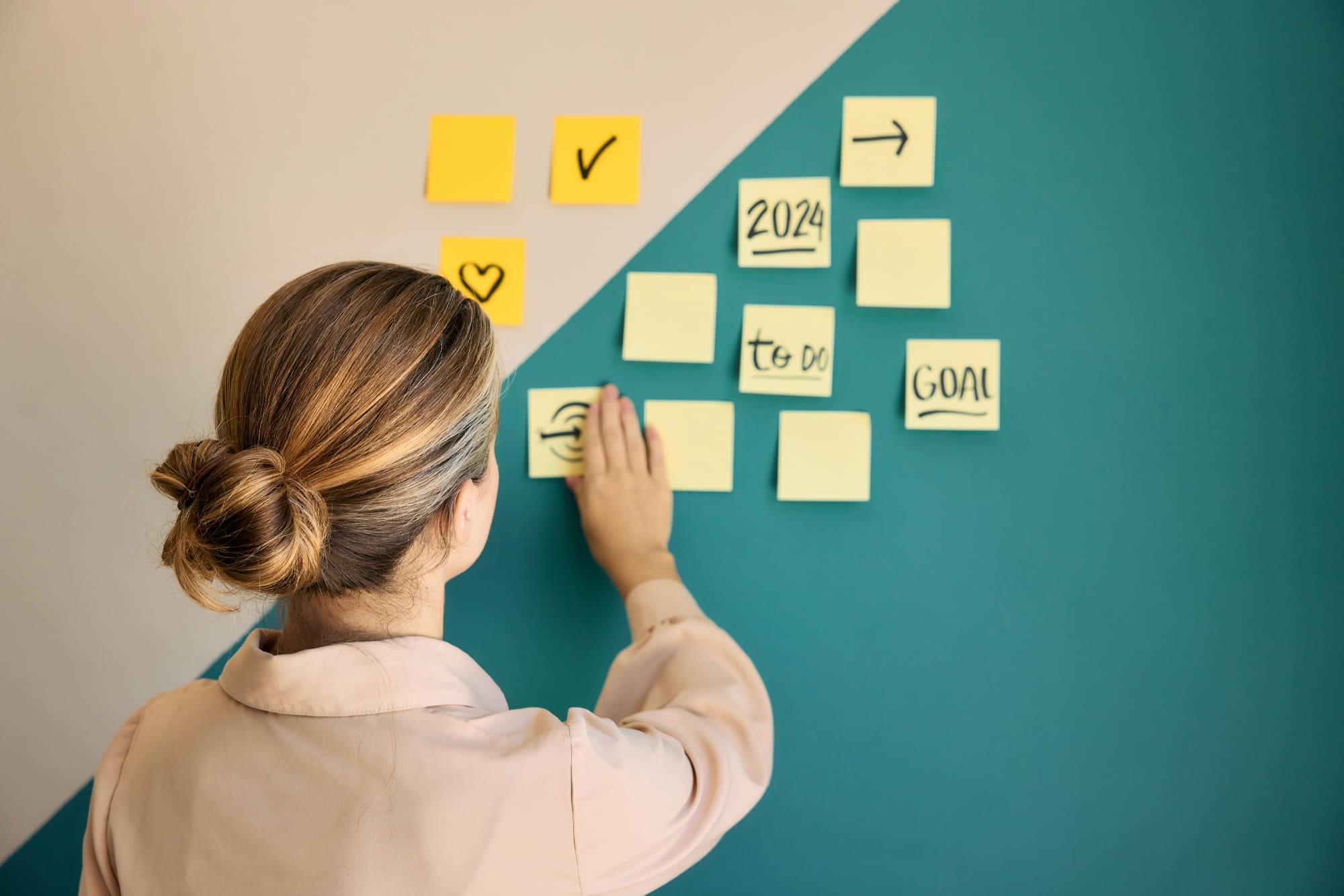 Sustainability Goals Woman putting goal-planning post-it notes on a green and cream wall.