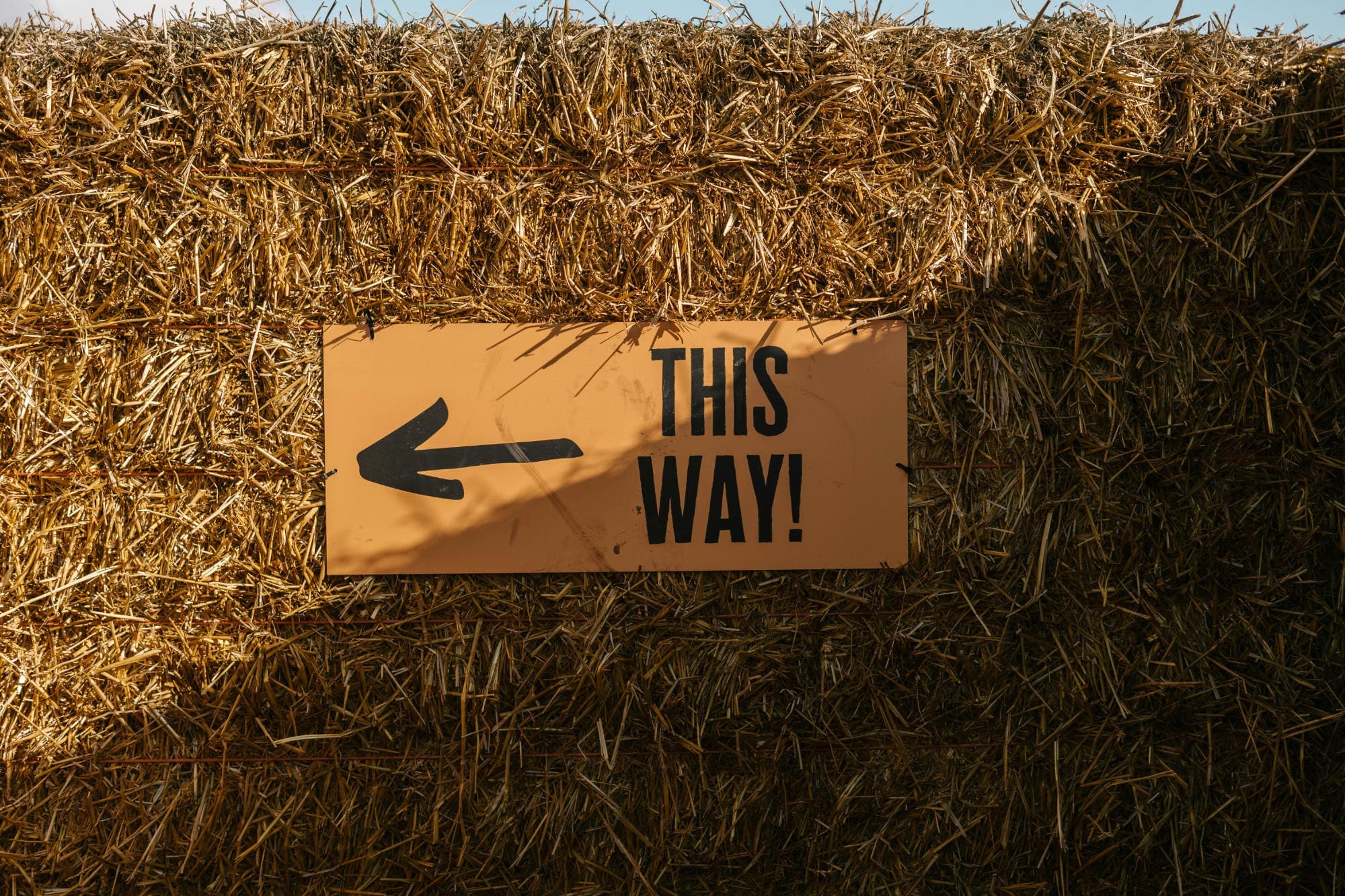 A sign saying 'this way' attached to a wall of hay.