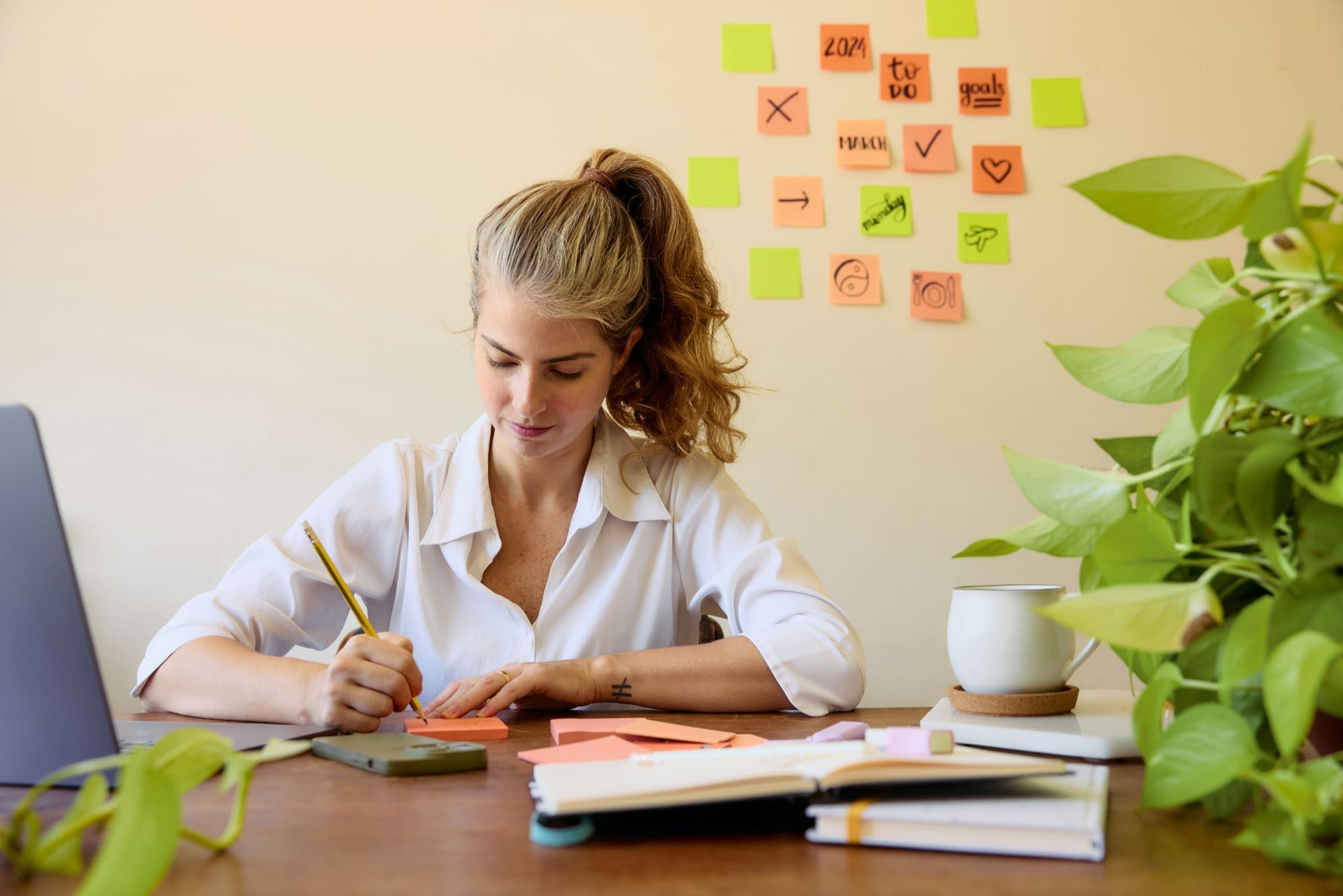 Where ESG Recruitment comes in Woman sitting at work desk with plant beside her and post-it notes stuck to wall in the background.