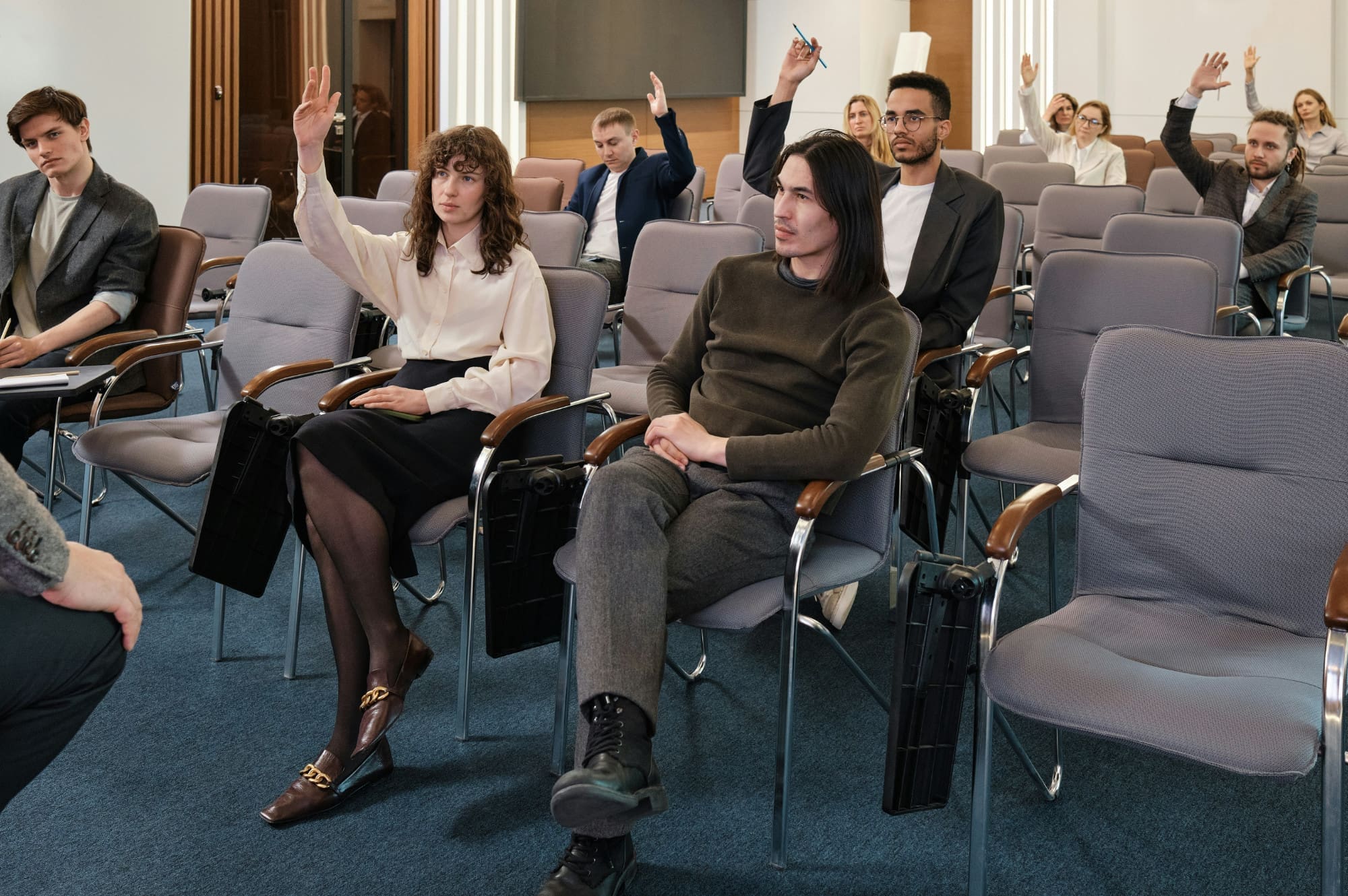 A room of professional-looking people with their hands in the air trying to answer a question.