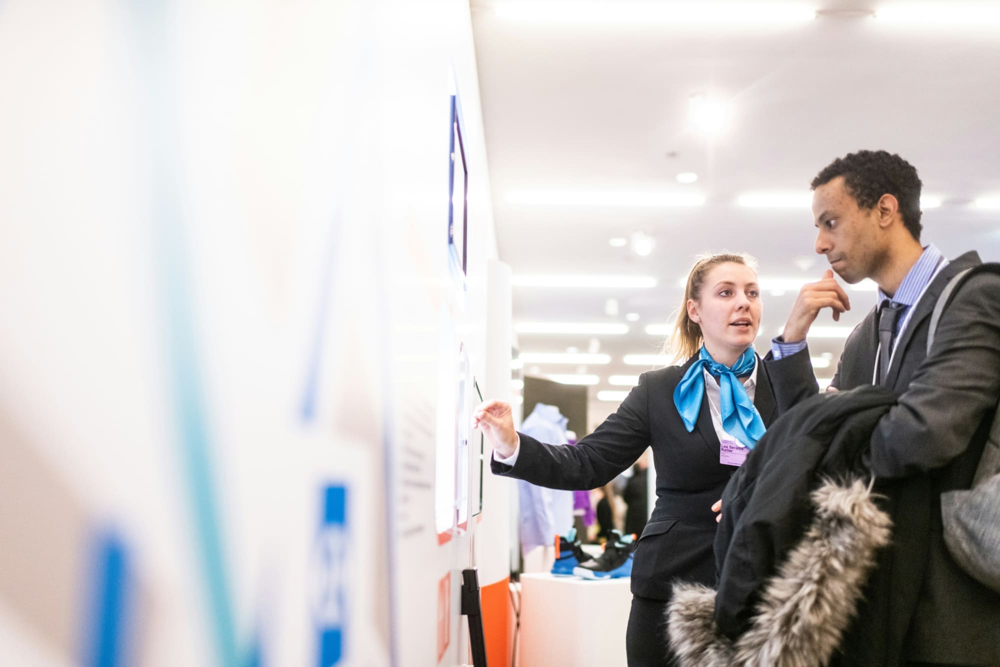 One office worker pointing at a white board to explain something to another office worker.