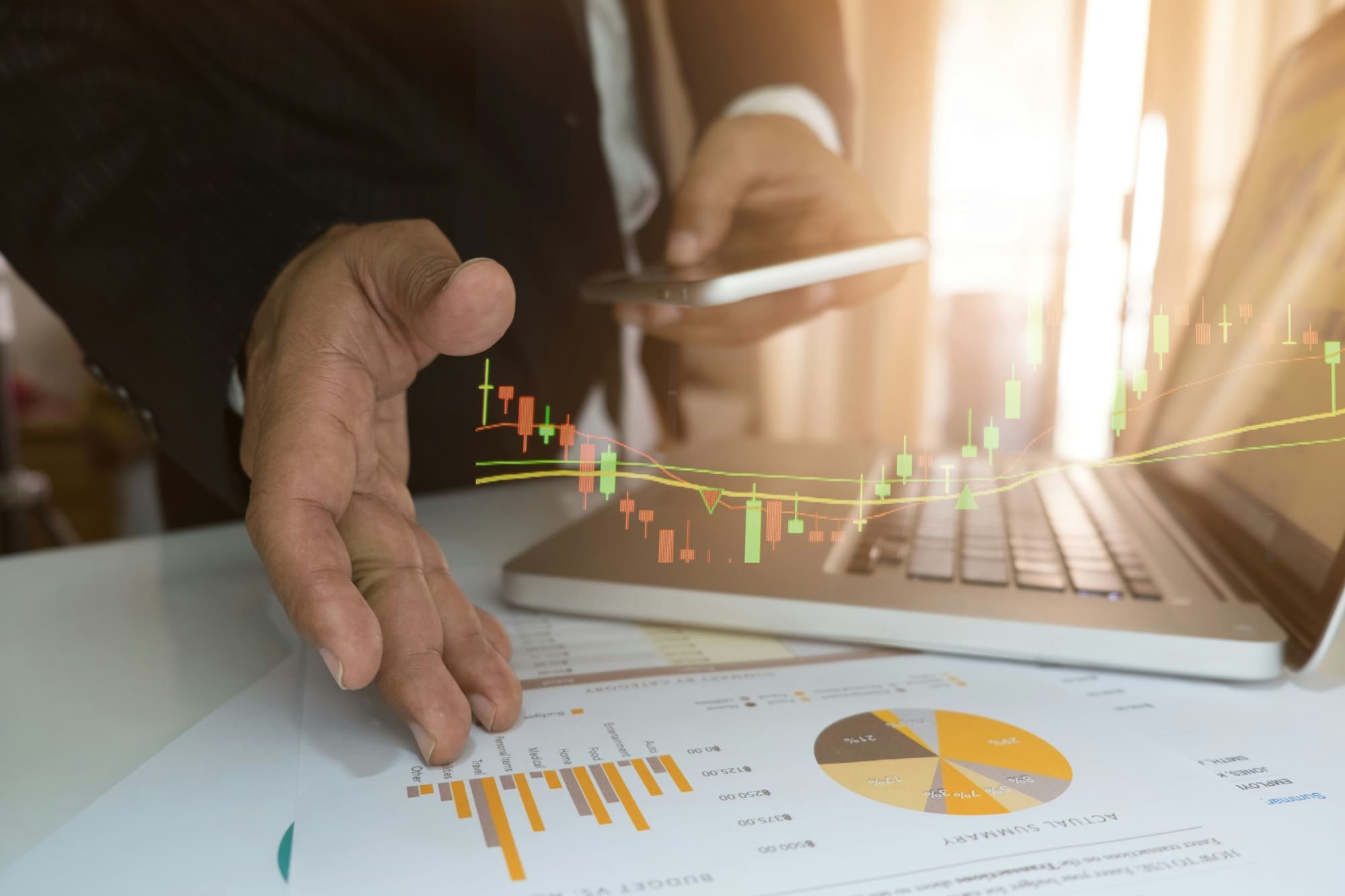 A man with hand above business charts and next to laptop, with a computer-generated depiction of the data from the charts entering the laptop.