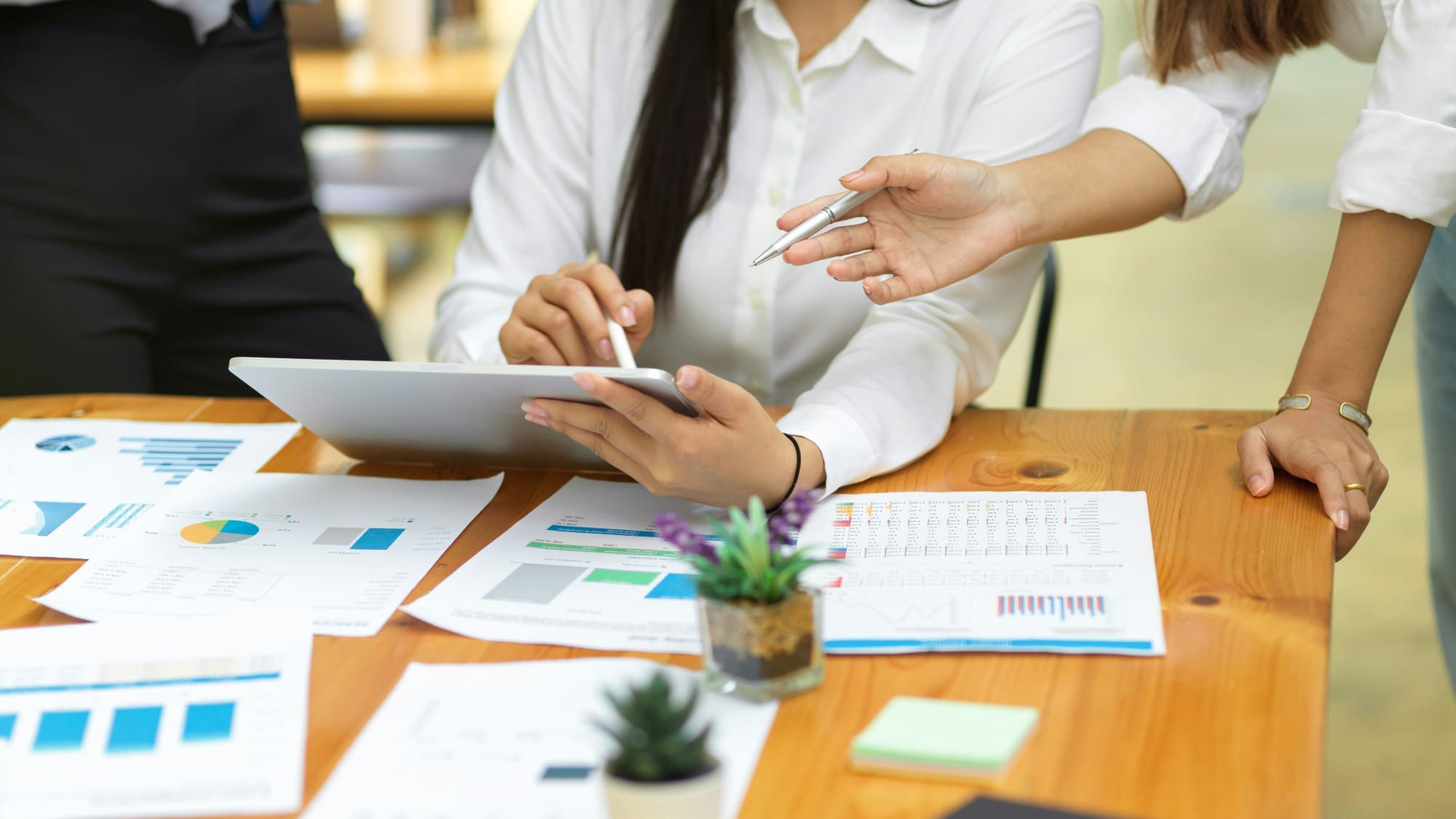 Two office workers next to desk covered in graphs, pointing at tablet.