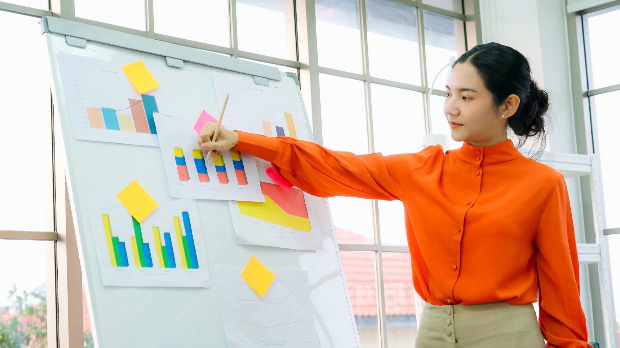 Why? A woman standing next to whiteboard using a pen to point at some bar charts.
