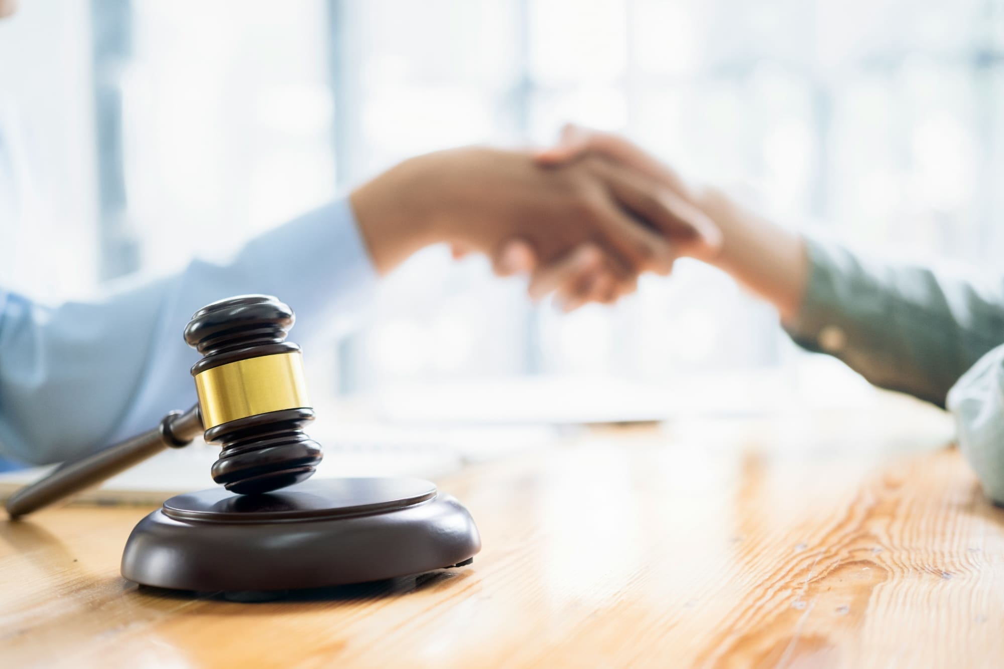 Backup Two people shaking hands in the background with a gavel in the foreground.