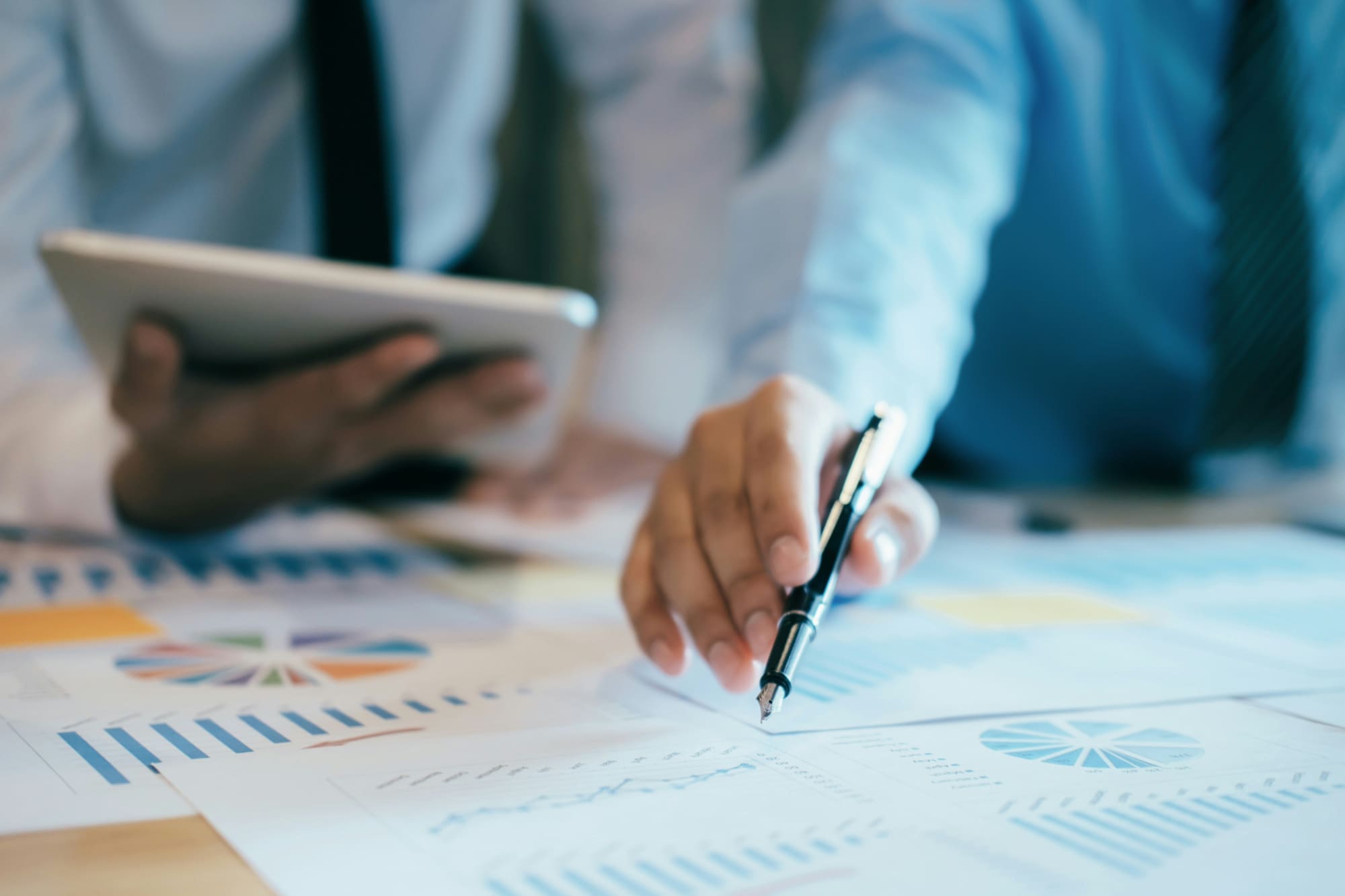 What this means A business person pointing at a printed chart while another one looks at a tablet.