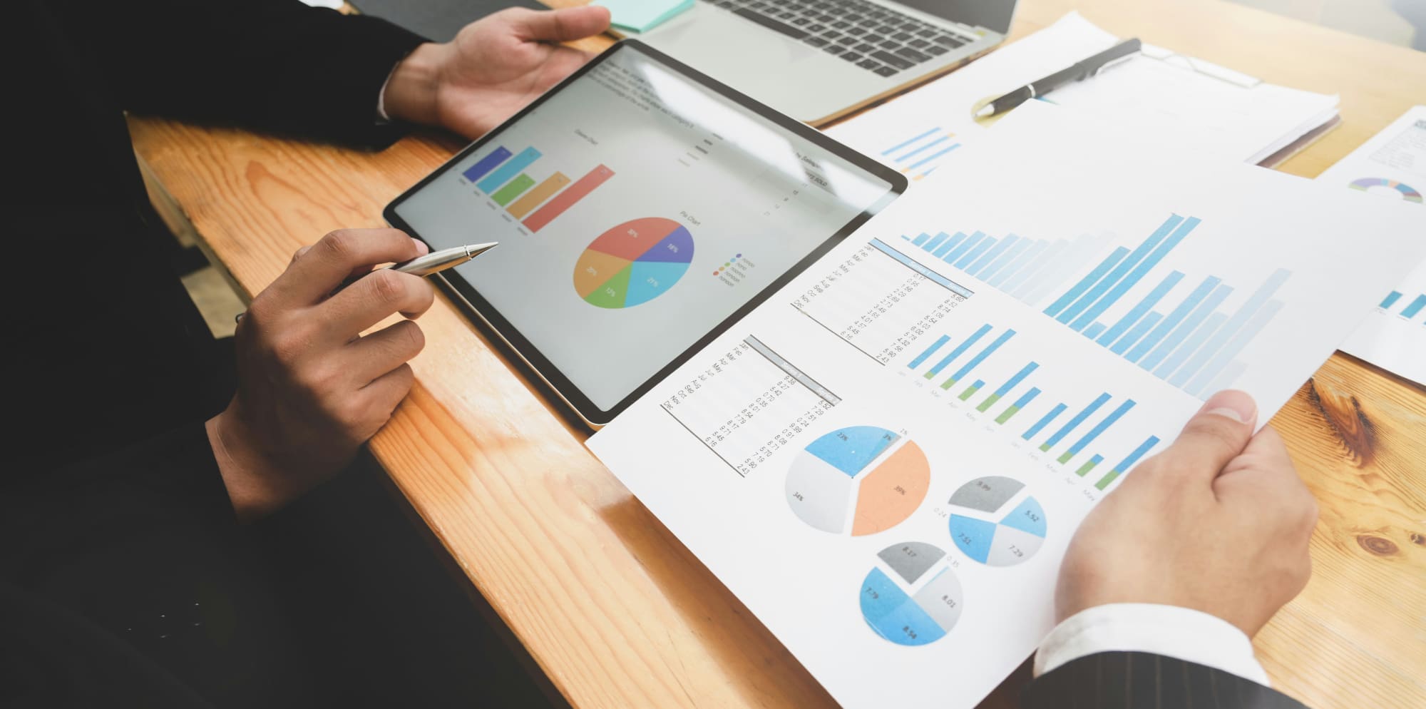 Which companies? Business people pointing at various charts printed out on paper and on a tablet.