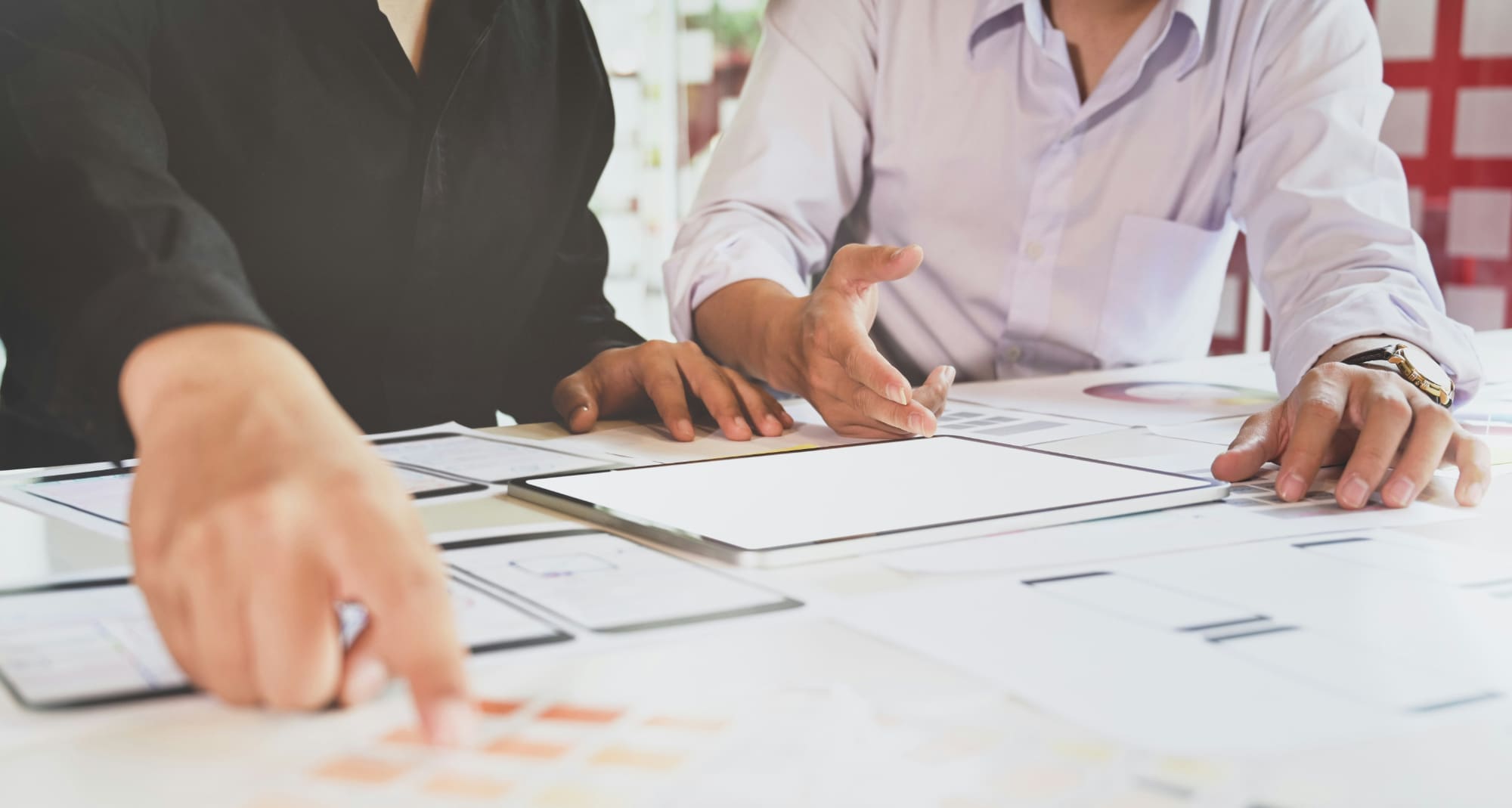 EcoVadis score losses Two people sat behind desk covered in paper documents with one person pointing out something to the other.