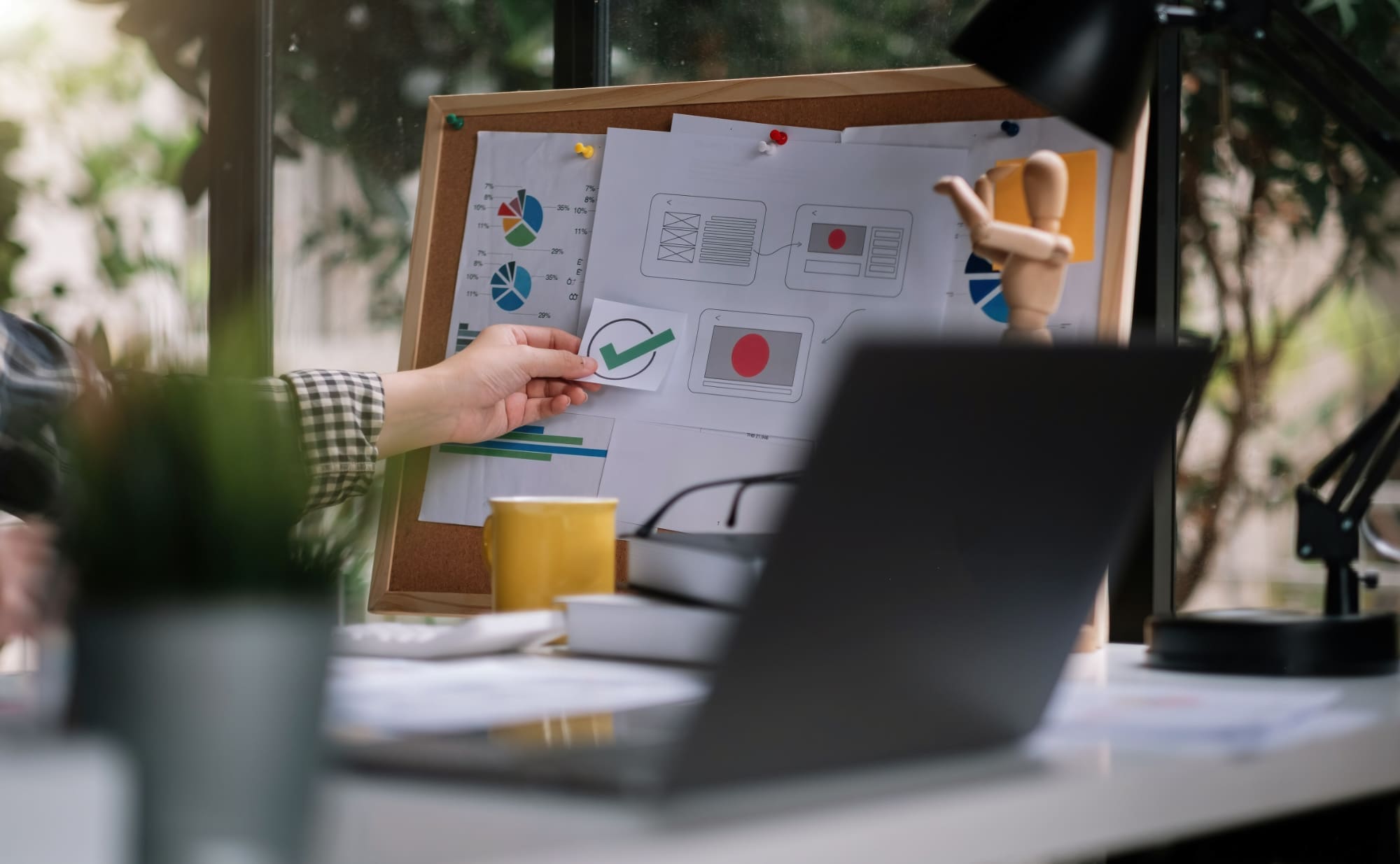 EcoVadis special cases Person placing 'ticked box' sticker onto a message board with laptop on desk in the foreground