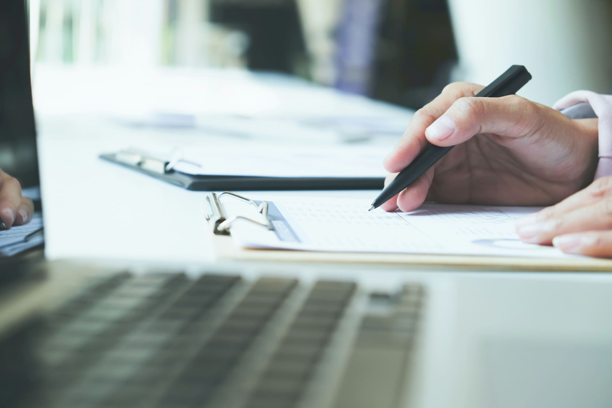 Understanding EcoVadis questionnaire Hand holding pen to search through EcoVadis questionnaire on desk next to laptop