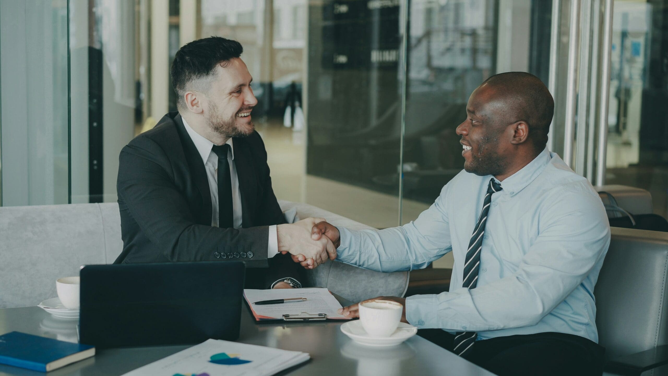 Two business professionals shaking hands over a meeting table, illustrating supplier partnership for collaborative Scope 3 decarbonisation